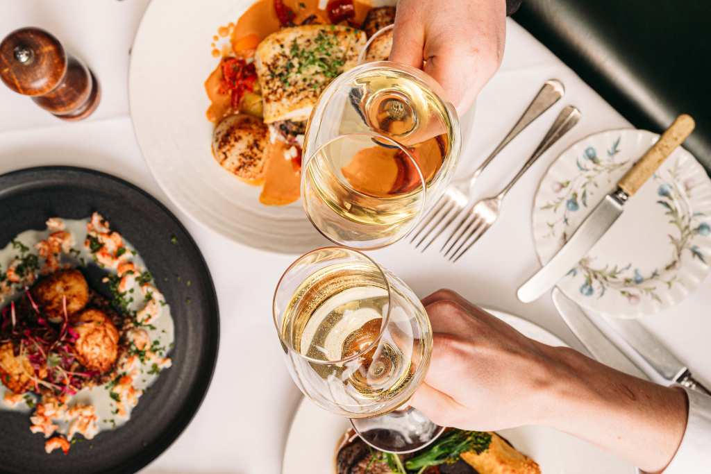 two people clinking glasses of wine over some food dishes